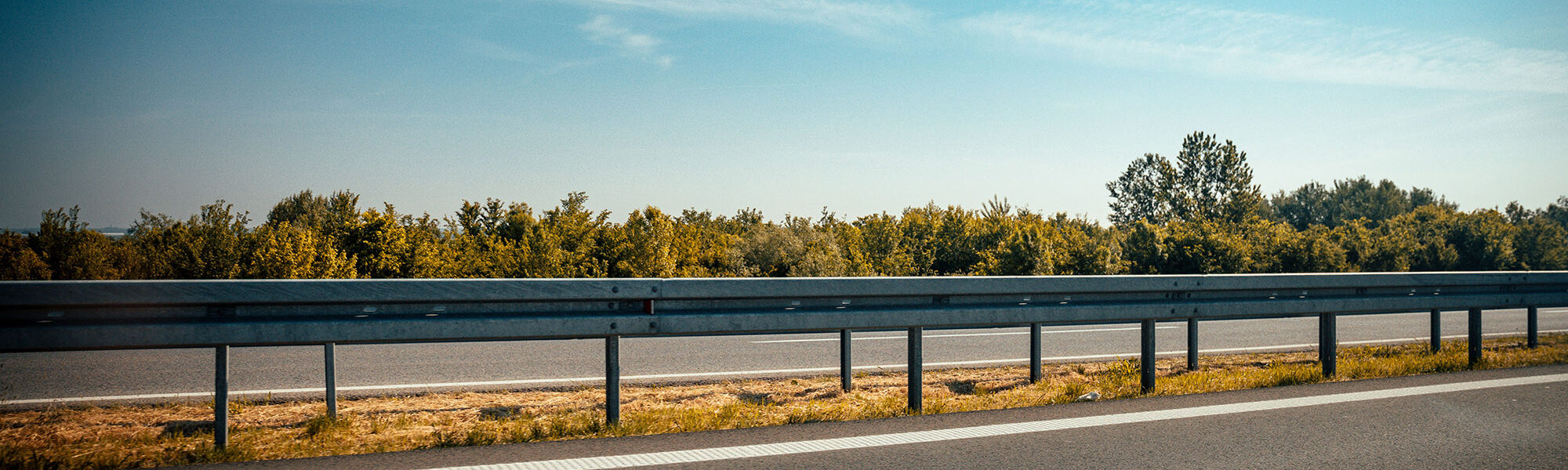 Beautiful shot of a highway guardrail on the side of a road with trees in the background A beautiful shot of a highway guardrail on the side of a road with trees in the background